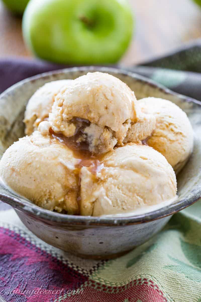 Scoops of apple cider ice cream in a bowl with a ribbon of boiled apple cider syrup drizzled over the top