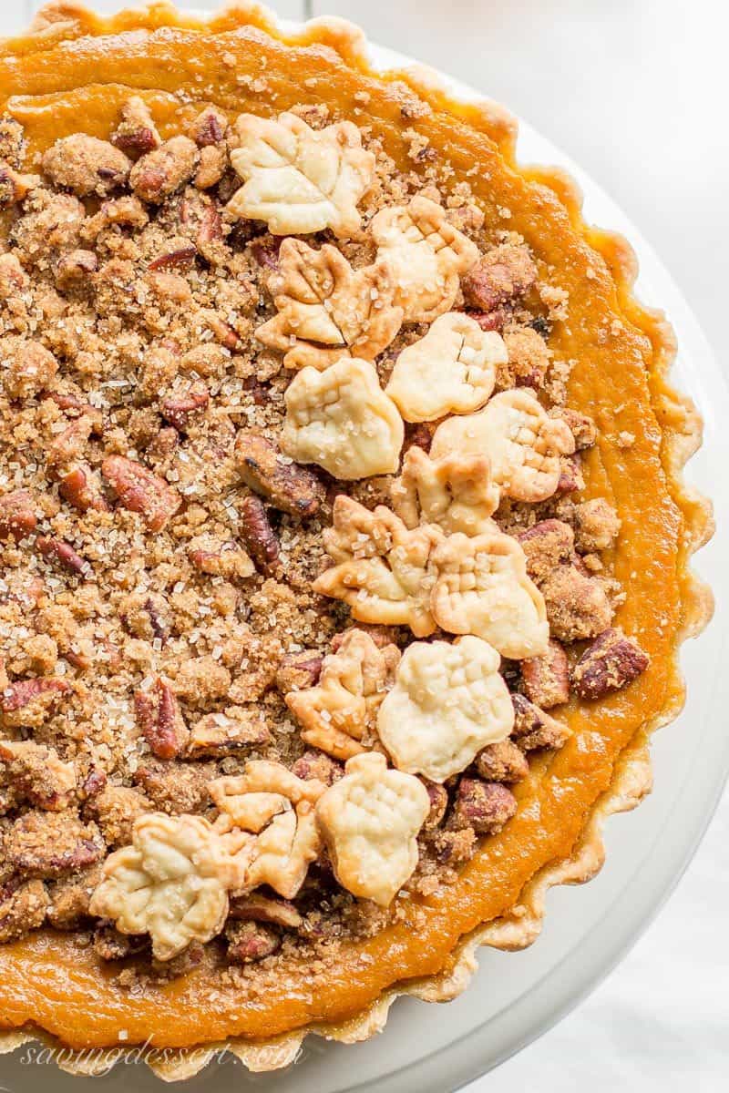 a closeup of a pumpkin tart with a pecan crumble topping garnished with pastry cut-outs of leaves and acorns.