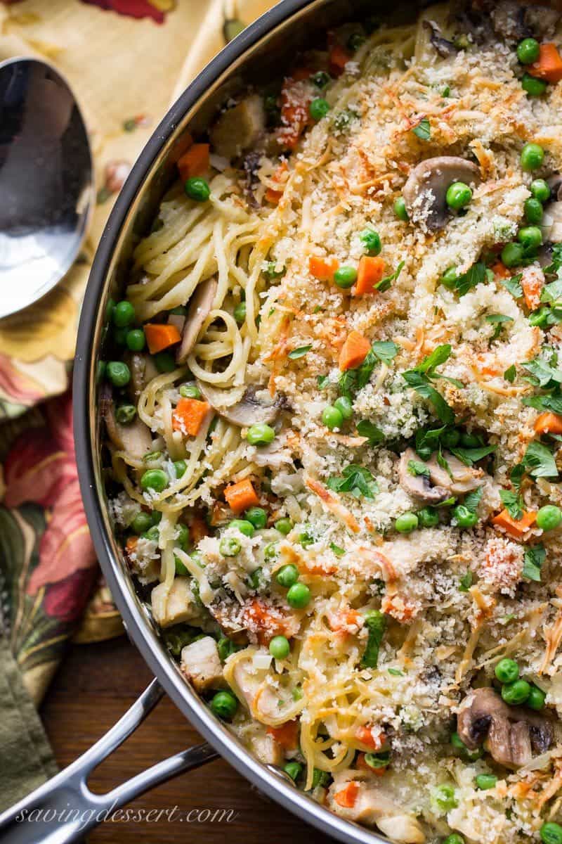 A large skillet full of turkey tetrazzini with peas, carrots, mushrooms and spaghetti noodles.