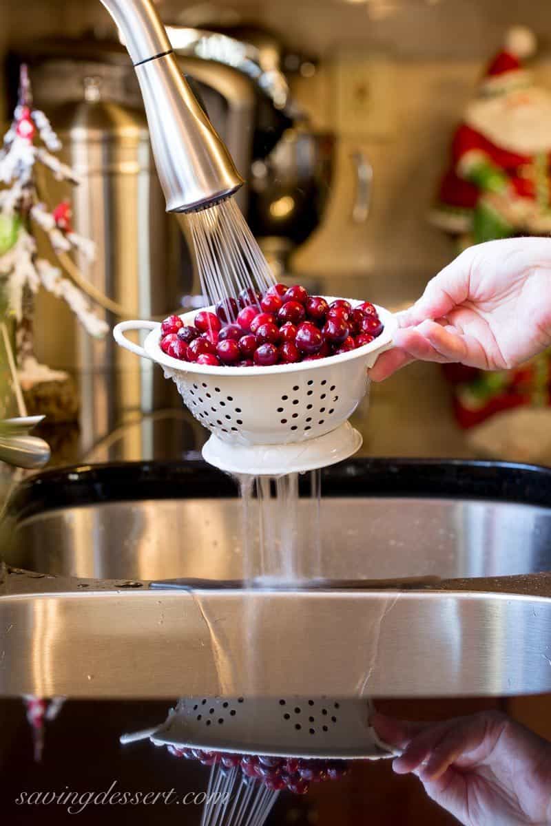 A colander full of cranberries over a sink and running faucet