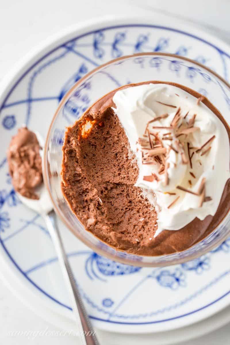 An overhead view of a bowl of fluffy chocolate mousse with whipped cream and chocolate shavings.