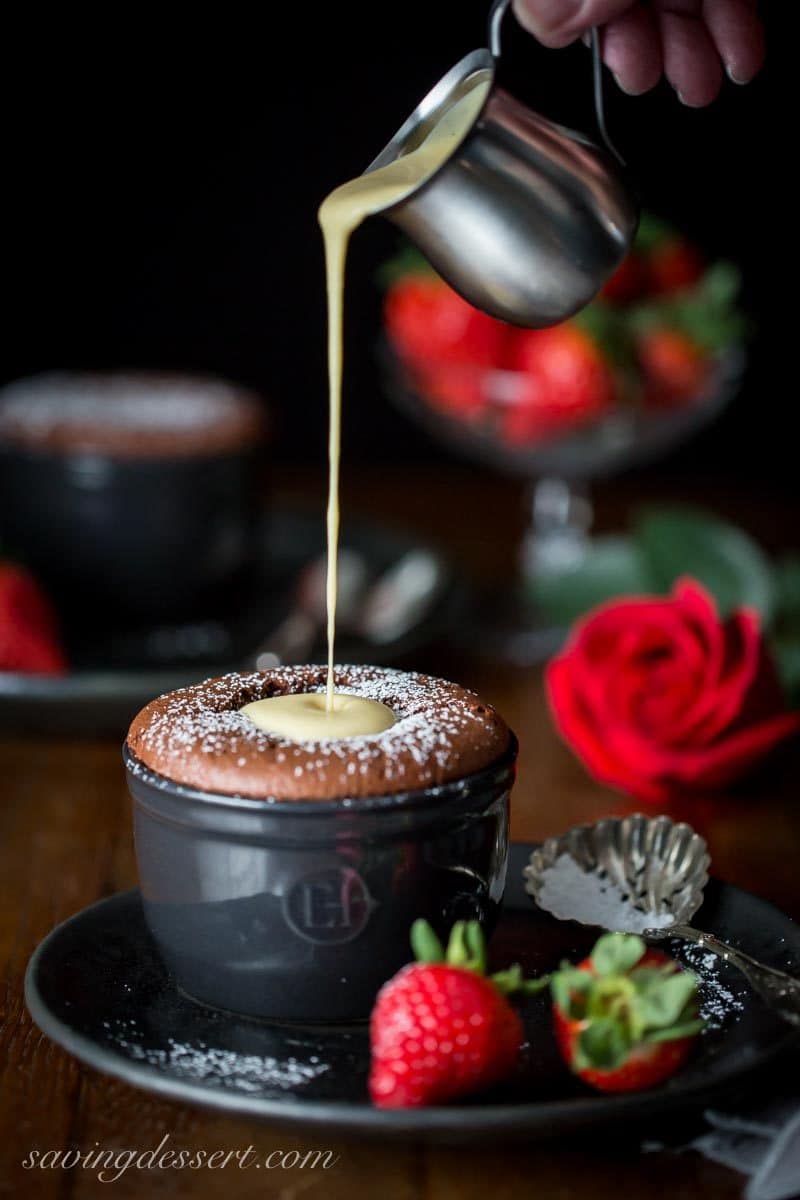 Pouring creme anglaise over an individual chocolate souffle with strawberries