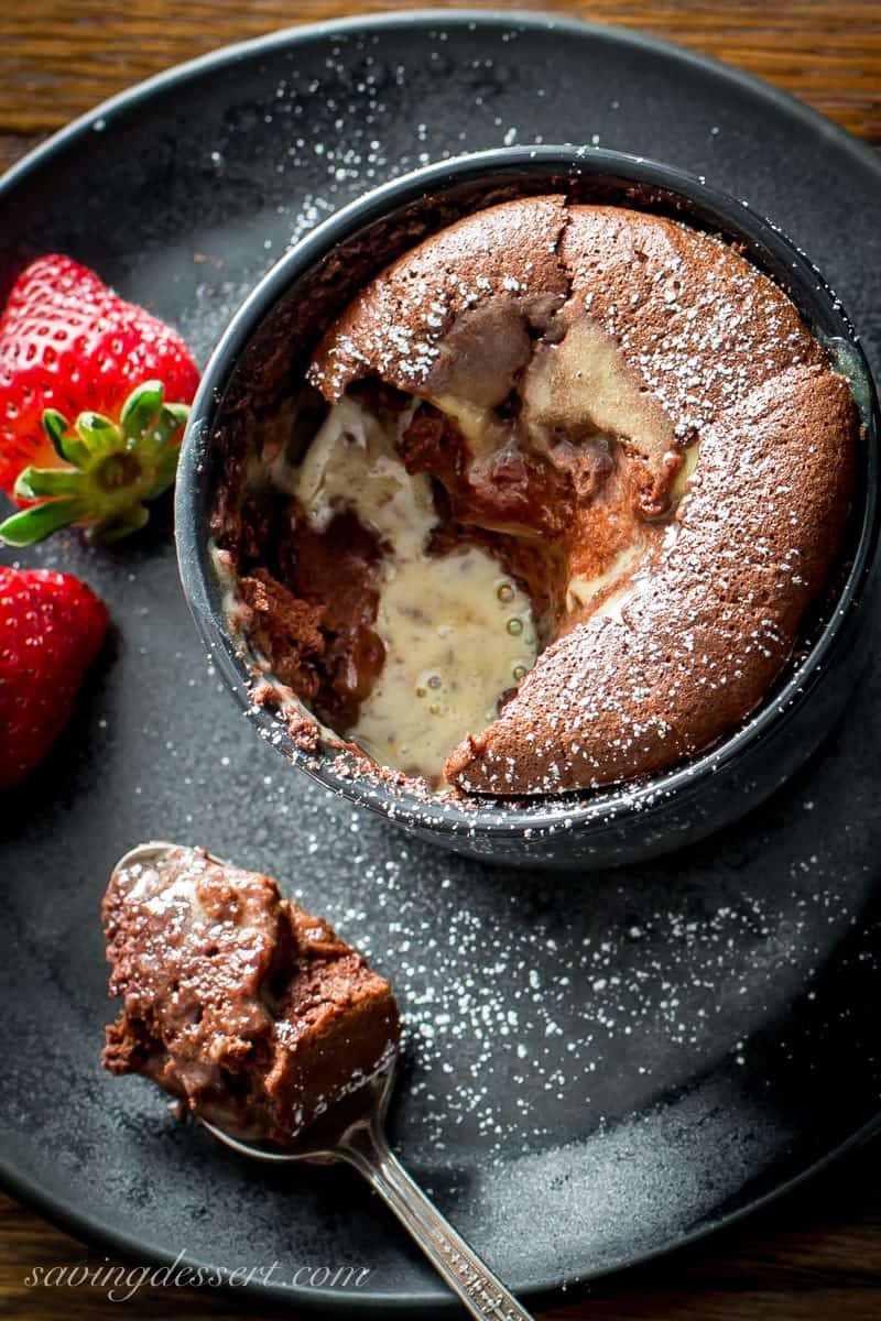 A cup of chocolate soufflé served with a creme anglaise and strawberries