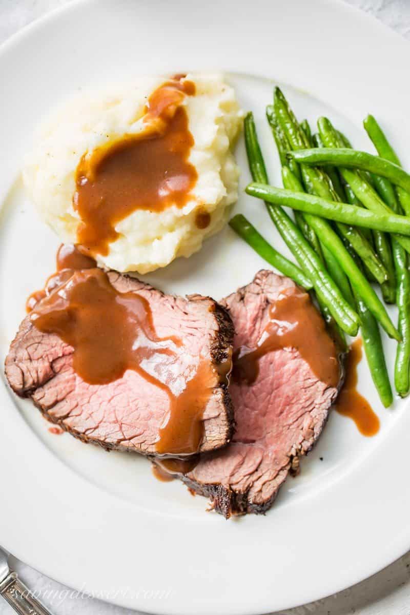 a plate with classic roast beef and gravy over mashed potatoes and green beans