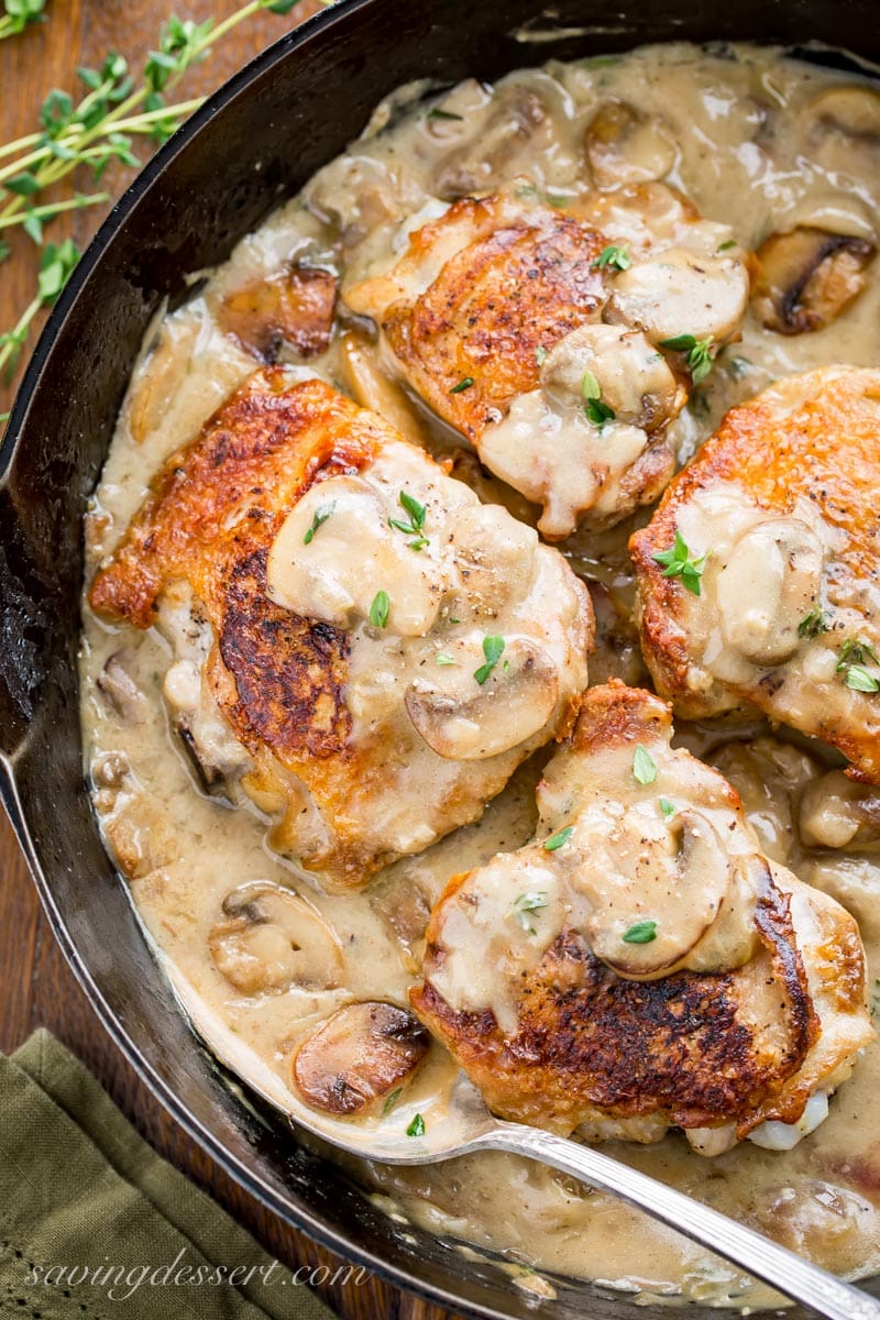 A skillet with crispy chicken thighs in a mushroom white wine pan sauce