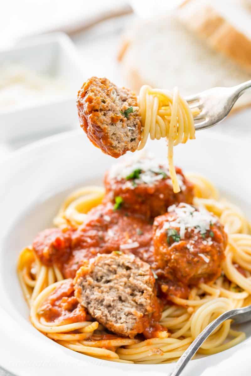 a forkful of spaghetti and half a meatball over a bowl of spaghetti using a homemade Italian Meatball recipe