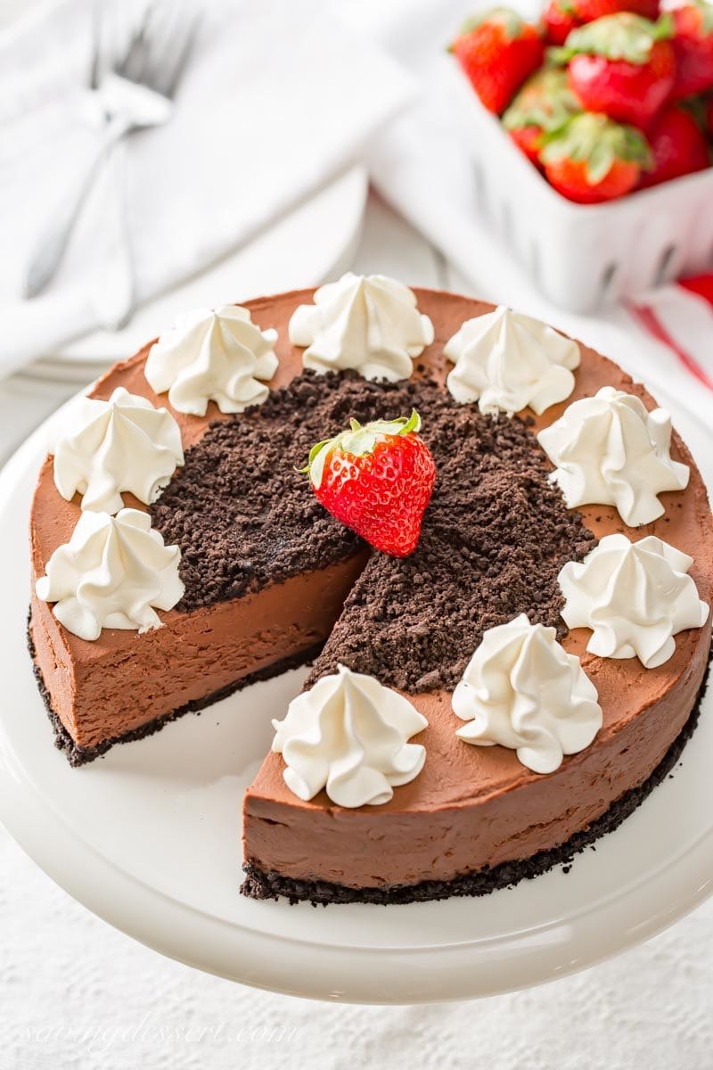 A sliced no-bake chocolate cheesecake topped with cookie crumbs, whipped cream and strawberries