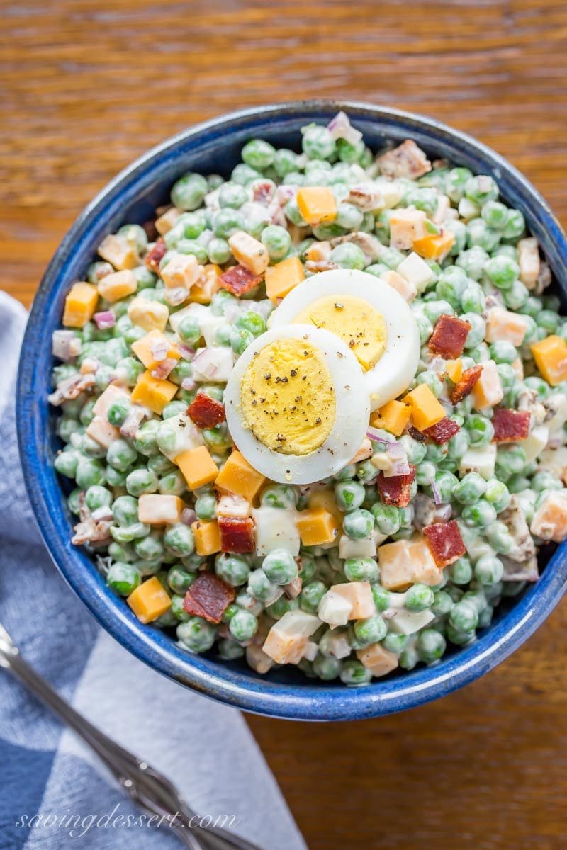 A blue bowl of English pea salad with boiled eggs, bacon and cheese