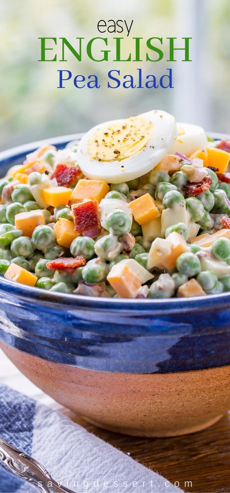 A bowl of pea salad with cheese, bacon and topped with a hard cooked egg