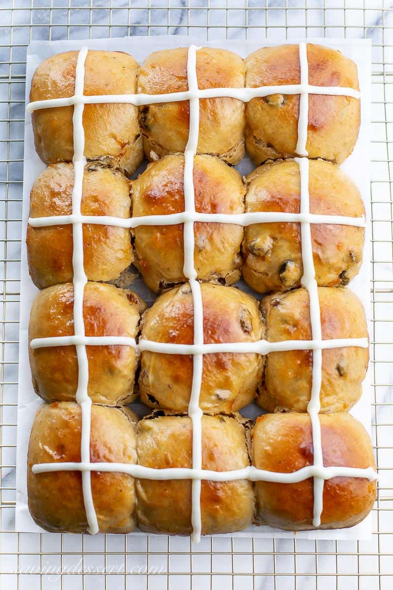 Overhead view of a cooling rack filled with a dozen hot cross buns with a cross on top made of icing