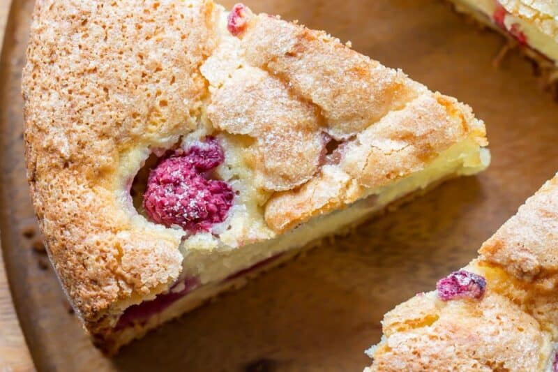 An overhead view of a sliced raspberry cake on a wooden cake platter.