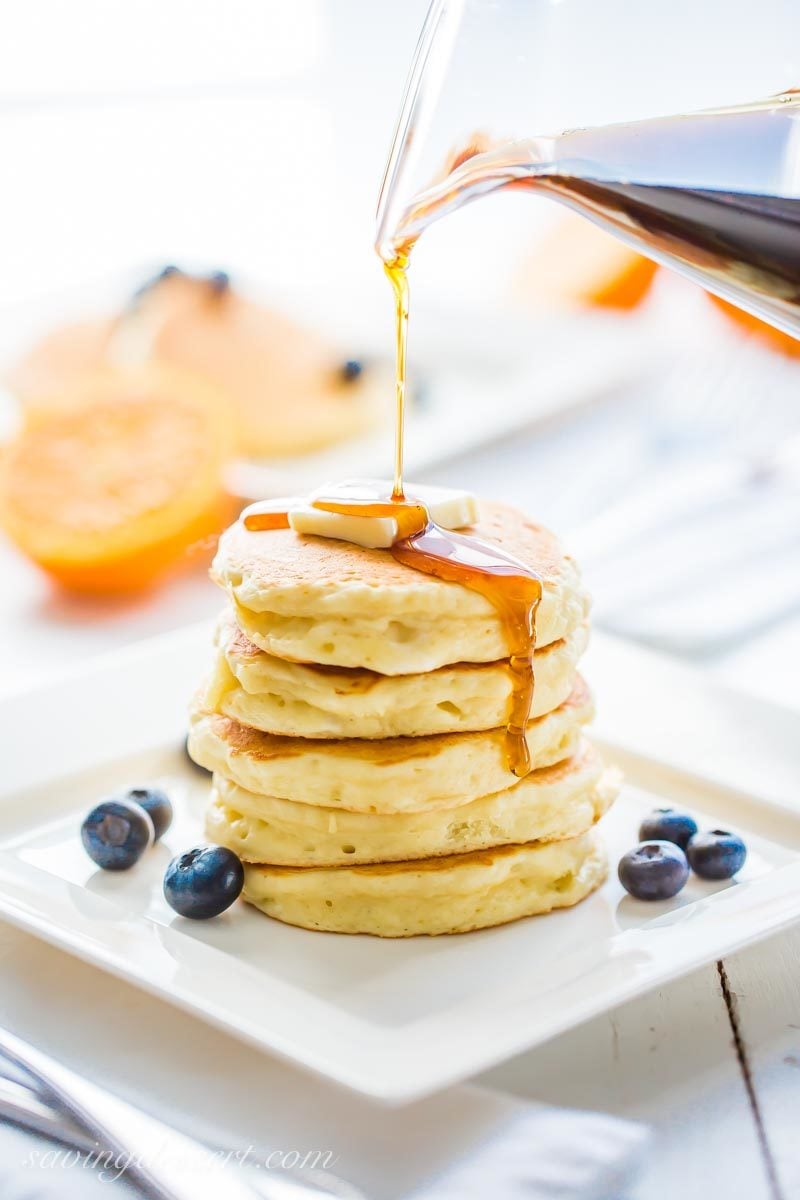 maple syrup being poured over a stack of ricotta pancakes