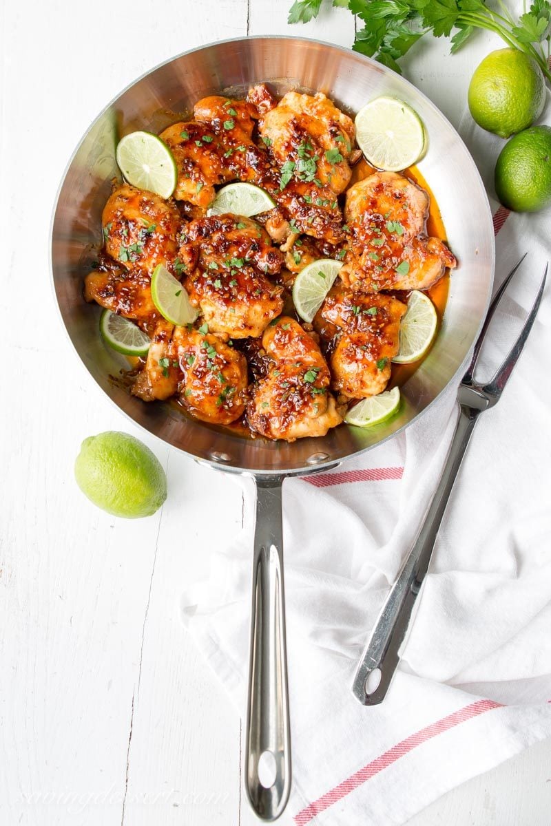 Skillet with chicken thighs coated in a garlic, lime, honey sauce garnished with lime wedges