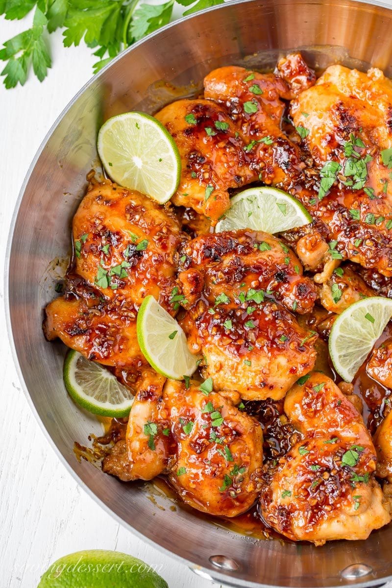 Boneless chicken thighs in a skillet with a sticky honey lime sauce and limes