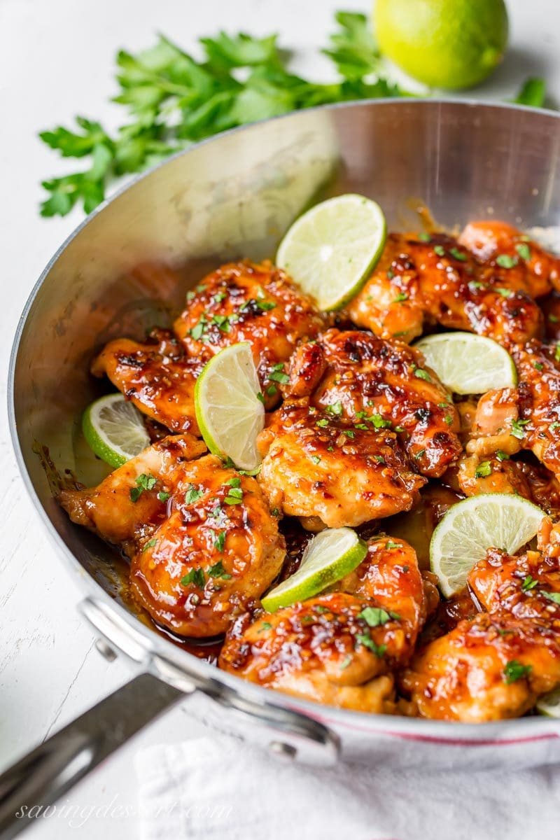 A skillet with chicken thighs in a sauce garnished with lime wedges and parsley