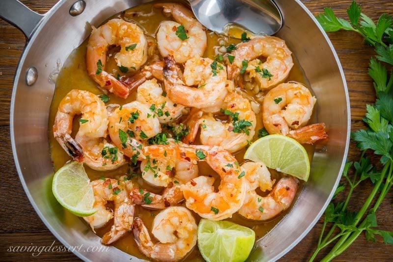 skillet with spicy shrimp in a honey lime sauce with fresh lime wedges and parsley