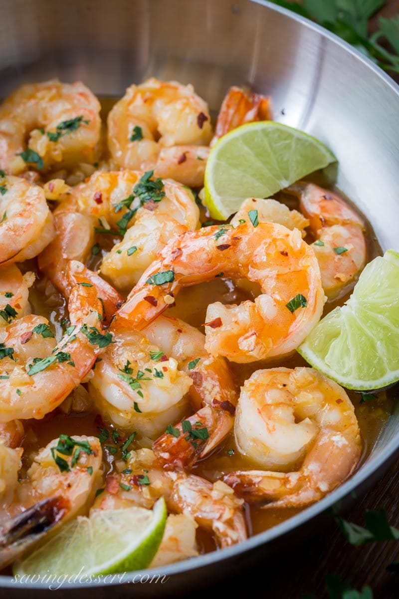 A skillet with spicy honey lime shrimp with lime wedges
