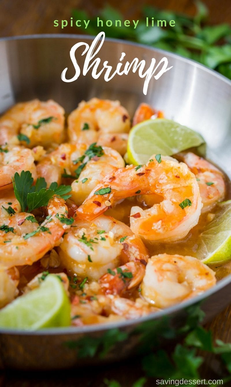 A skillet filled with shrimp with tails on garnished with lime wedges