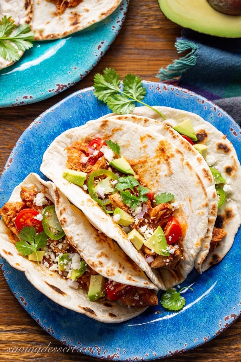 shredded chicken tinga tacos with avocado, tomatoes, jalapeño peppers, cilantro and crumbled Cojita cheese