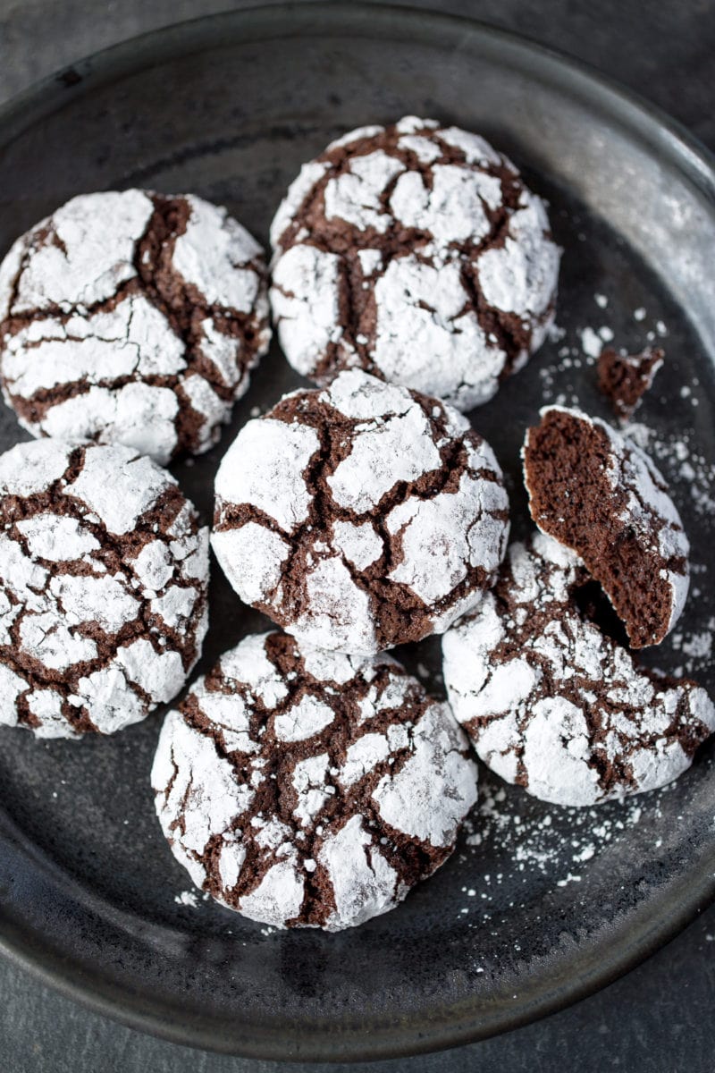 A black plate with powder sugar covered chocolate cookies