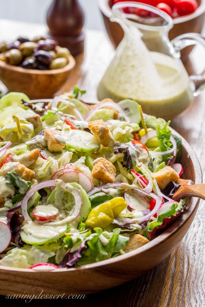 A wooden salad bowl filled with lettuce, radishes, peppers and onions drizzled with creamy Italian dressing.