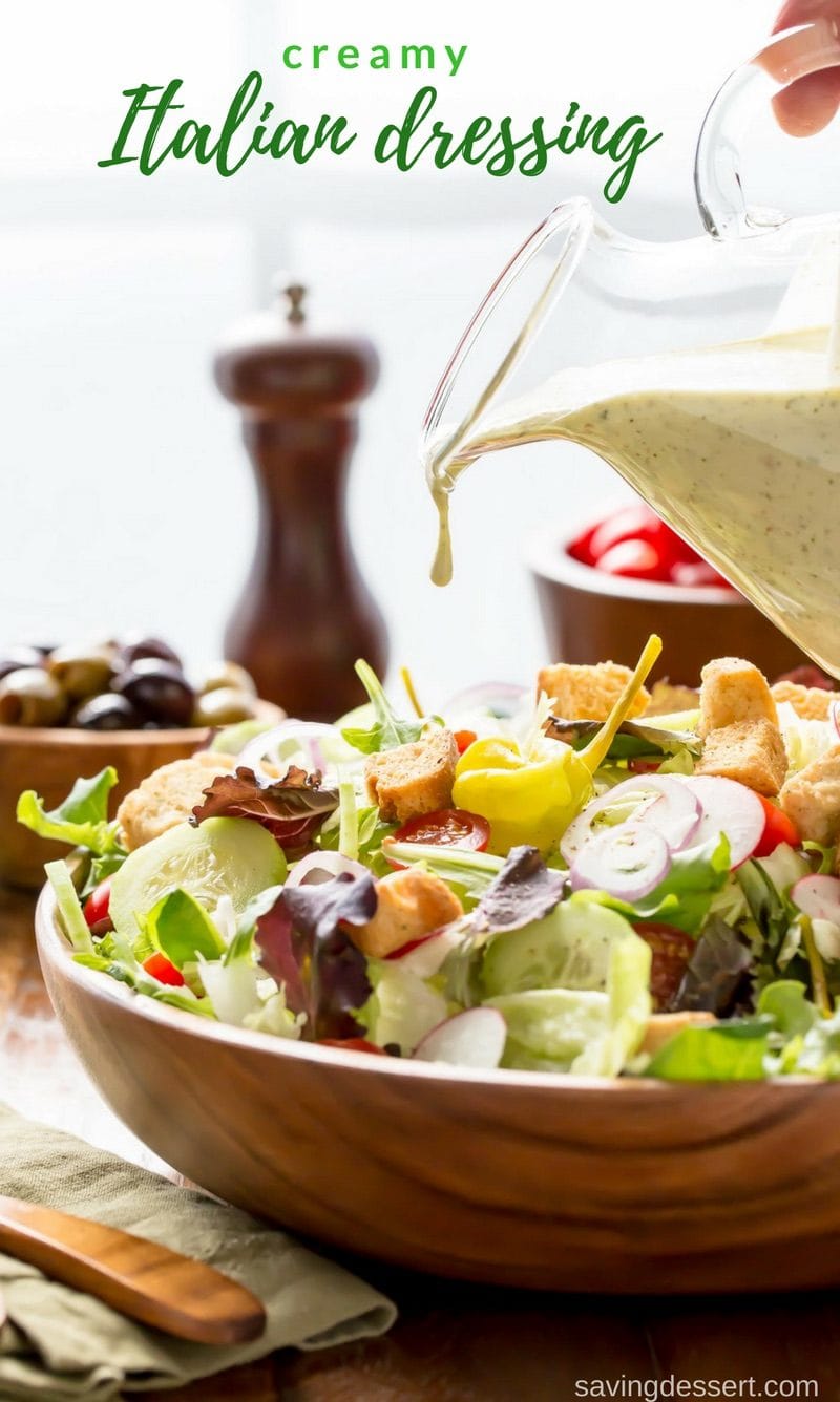 A large wooden bowl filled with salad and drizzled with a creamy Italian dressing