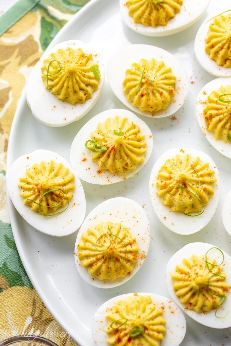 a platter of deviled eggs garnished with sliced green onions and paprika