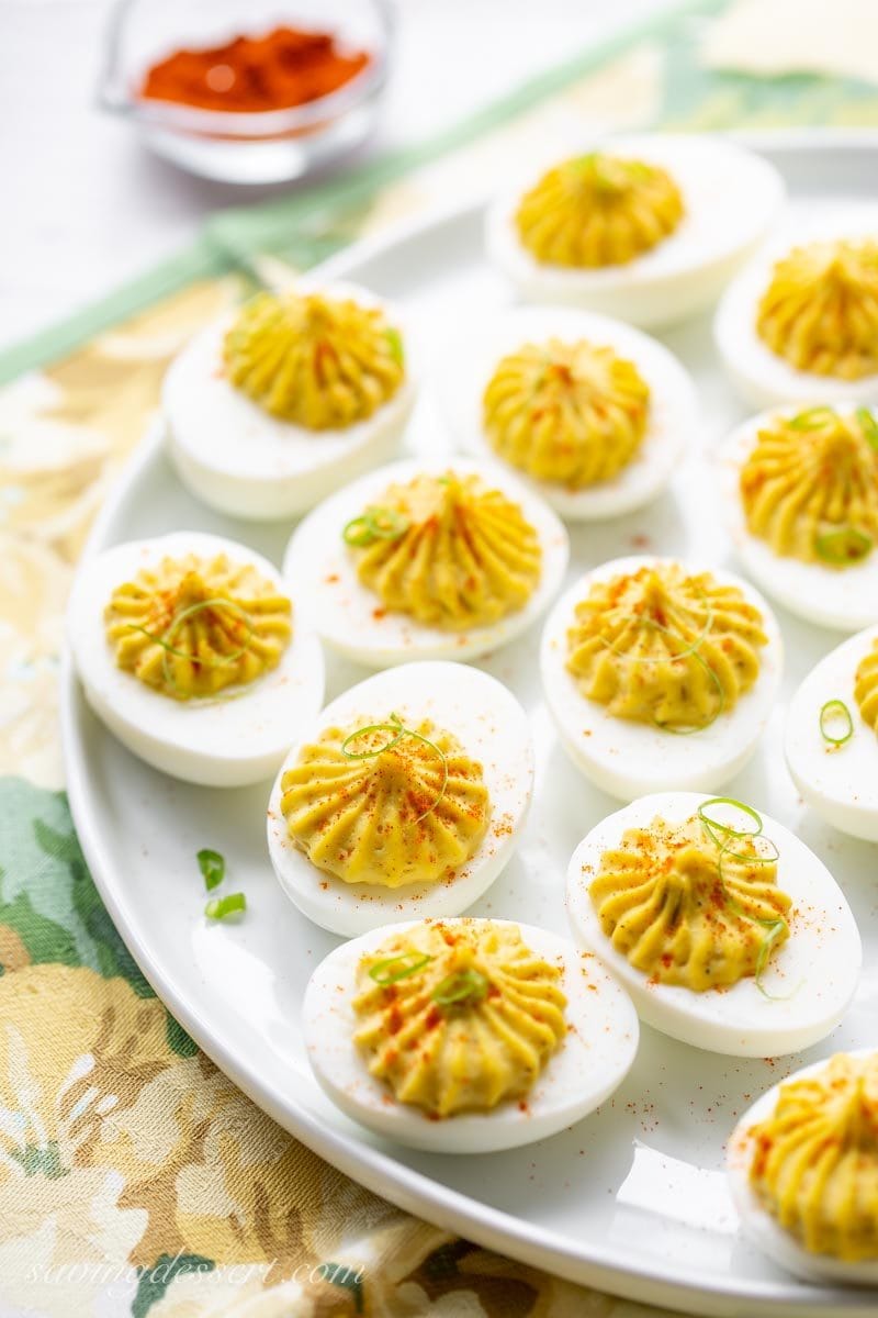 a plate of deviled eggs with sliced green onions garnished with paprika