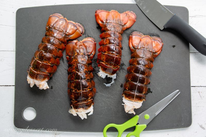 4 Lobster tails on a cutting board with a knife and scissors.