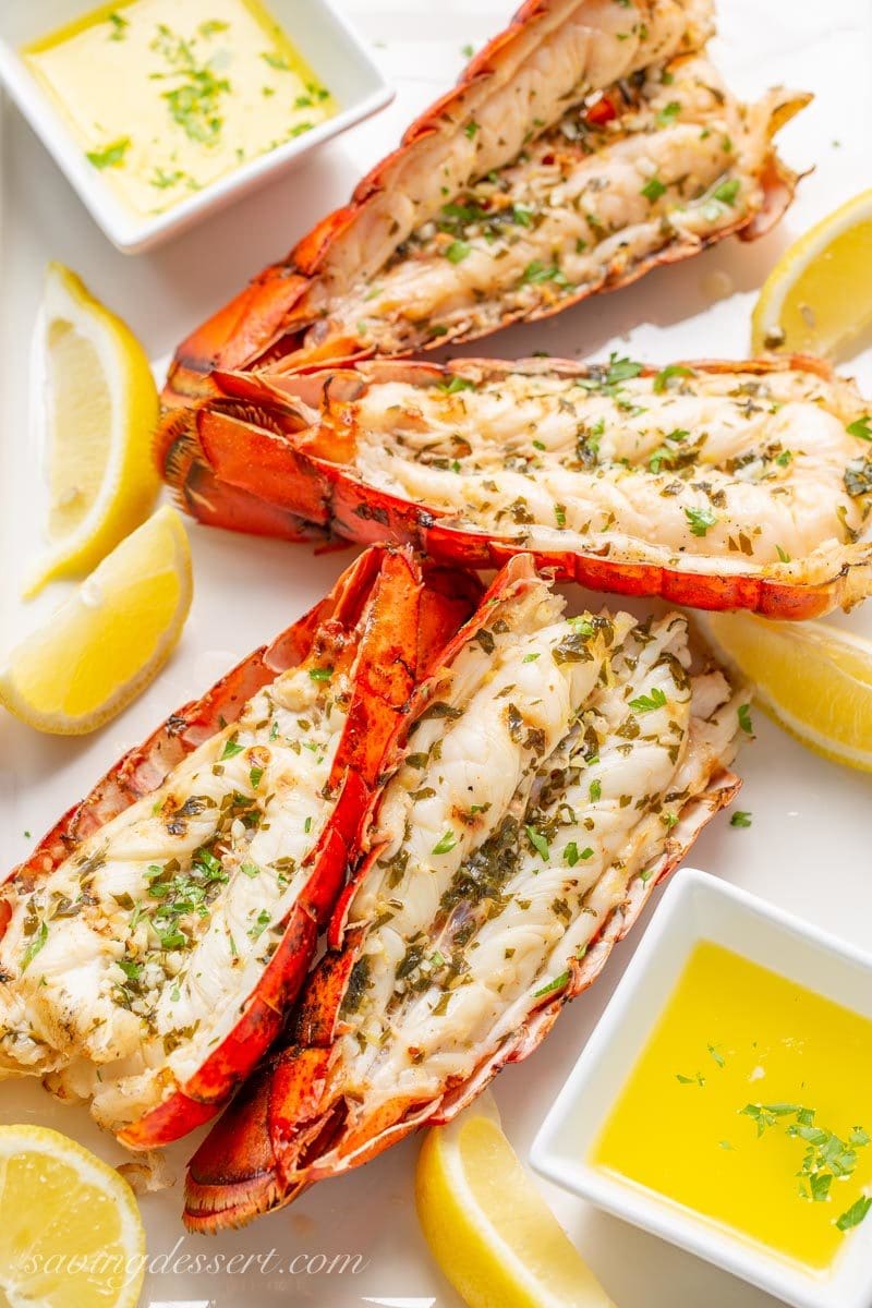 grilled lobster tails on a platter with melted butter and lemon wedges