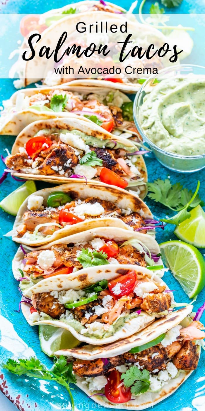 A large platter of grilled salmon tacos in a line. Topped with fresh tomatoes and served with lime wedges