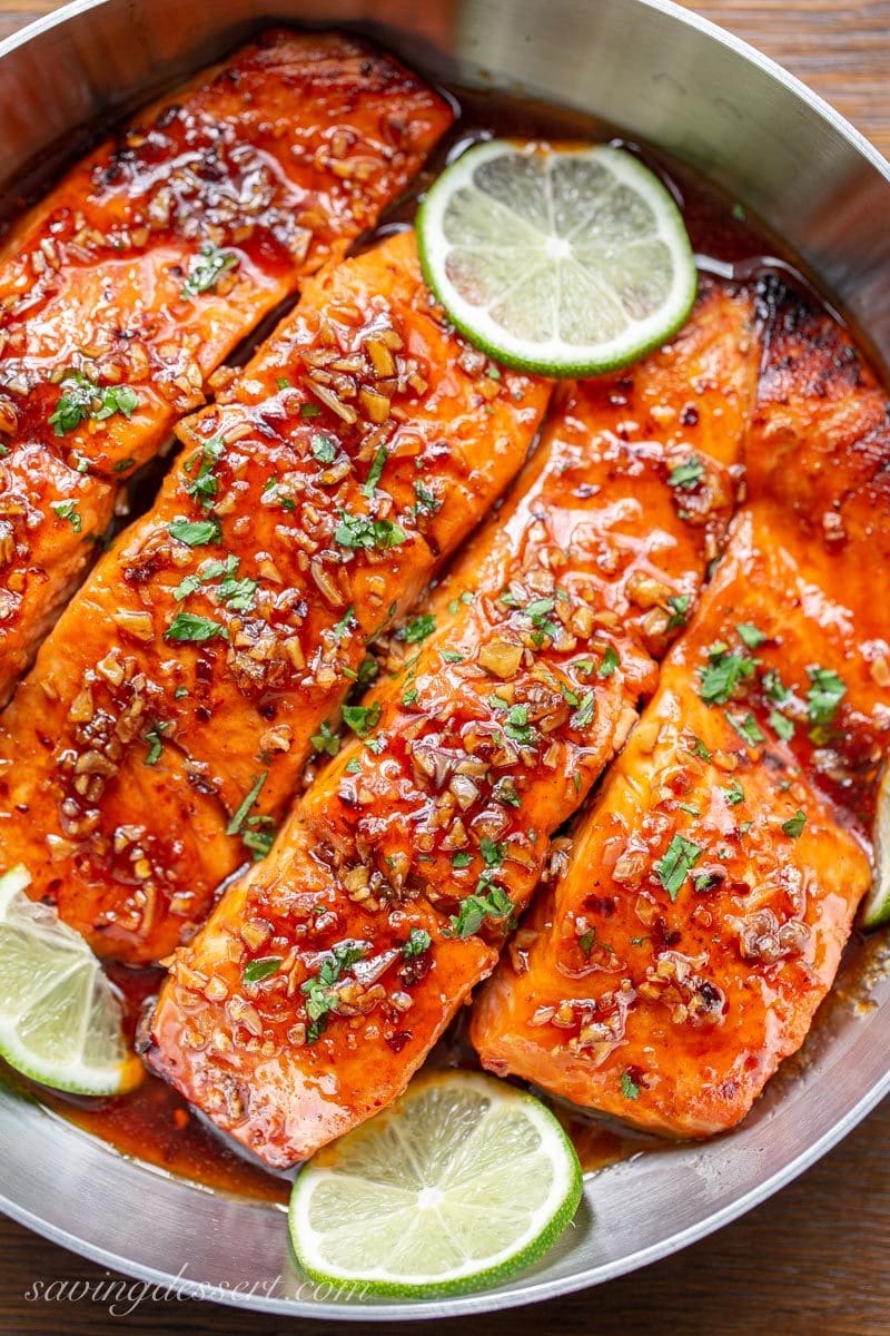 A skillet with 4 pieces of salmon topped with garlic, parsley and lime