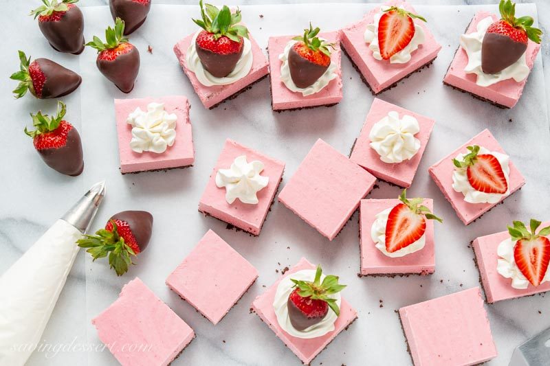 Strawberry Cheesecake Bars decorated with whipped cream, sliced strawberries and chocolate covered strawberries.