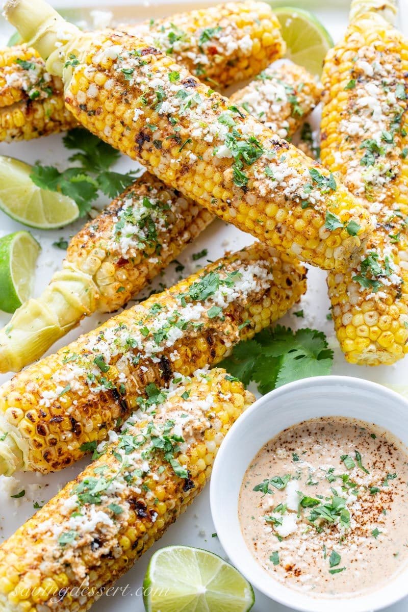 Ears of grilled Mexican Street Corn on a platter with a spicy sauce served on the side