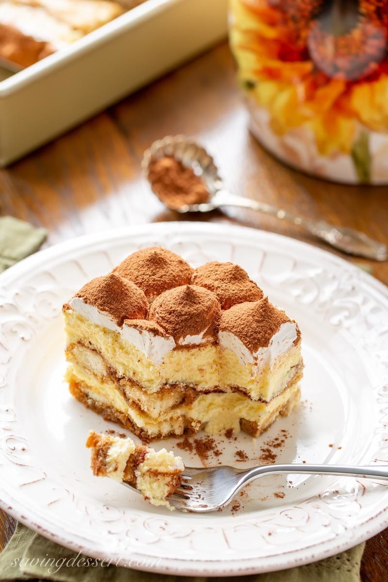 A piece of Tiramisu dusted with cocoa with a bite taken out with a fork