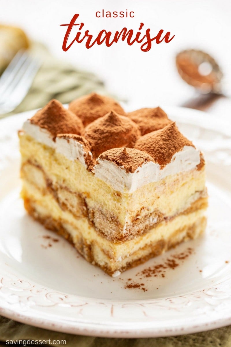 A slice of classic Tiramisu topped with mounds of whipped cream and cocoa powder