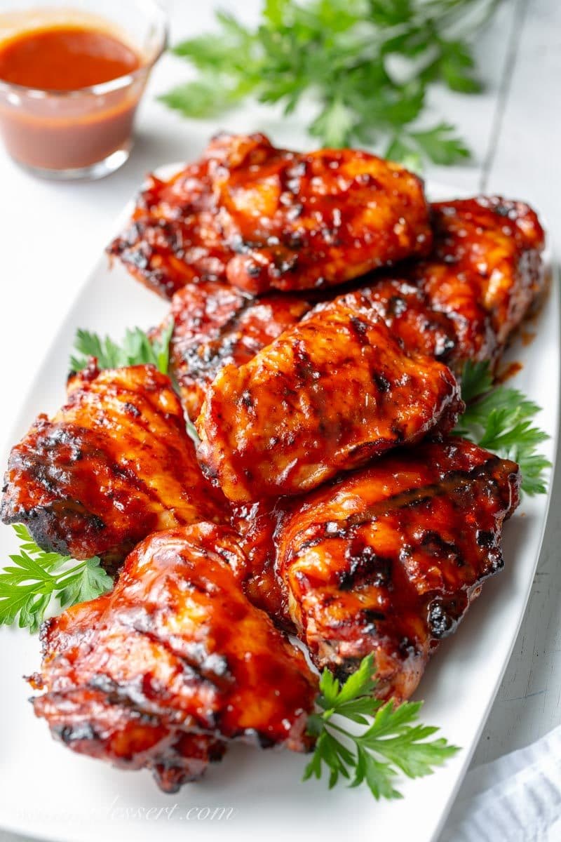 A plate of grilled barbecued chicken thighs with sauce and parsley