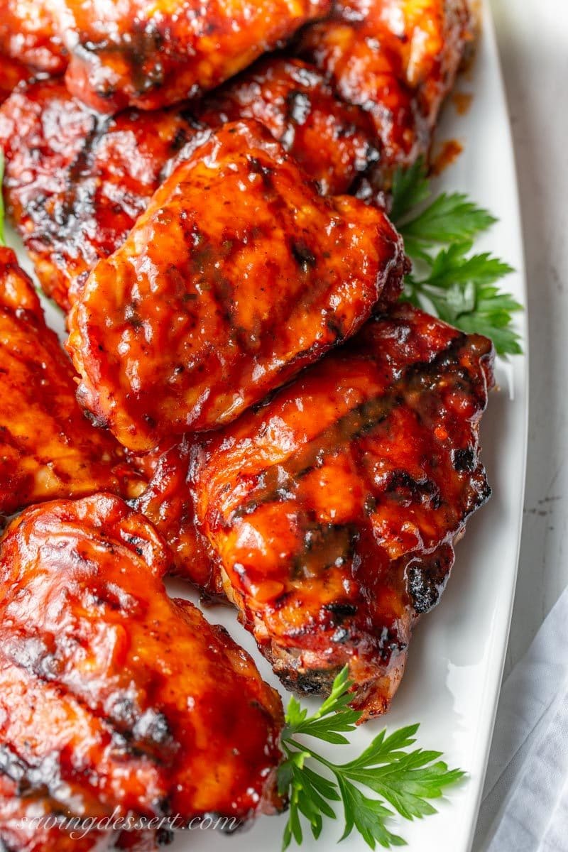 A close up of grilled Barbecued Chicken Thighs with a rich red sauce and garnished with parsley