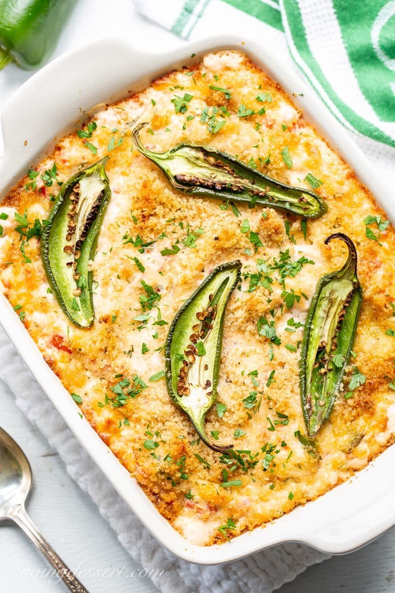 A small casserole with hot, bubbly Jalapeño Popper Dip topped with sliced jalapeños and parsley