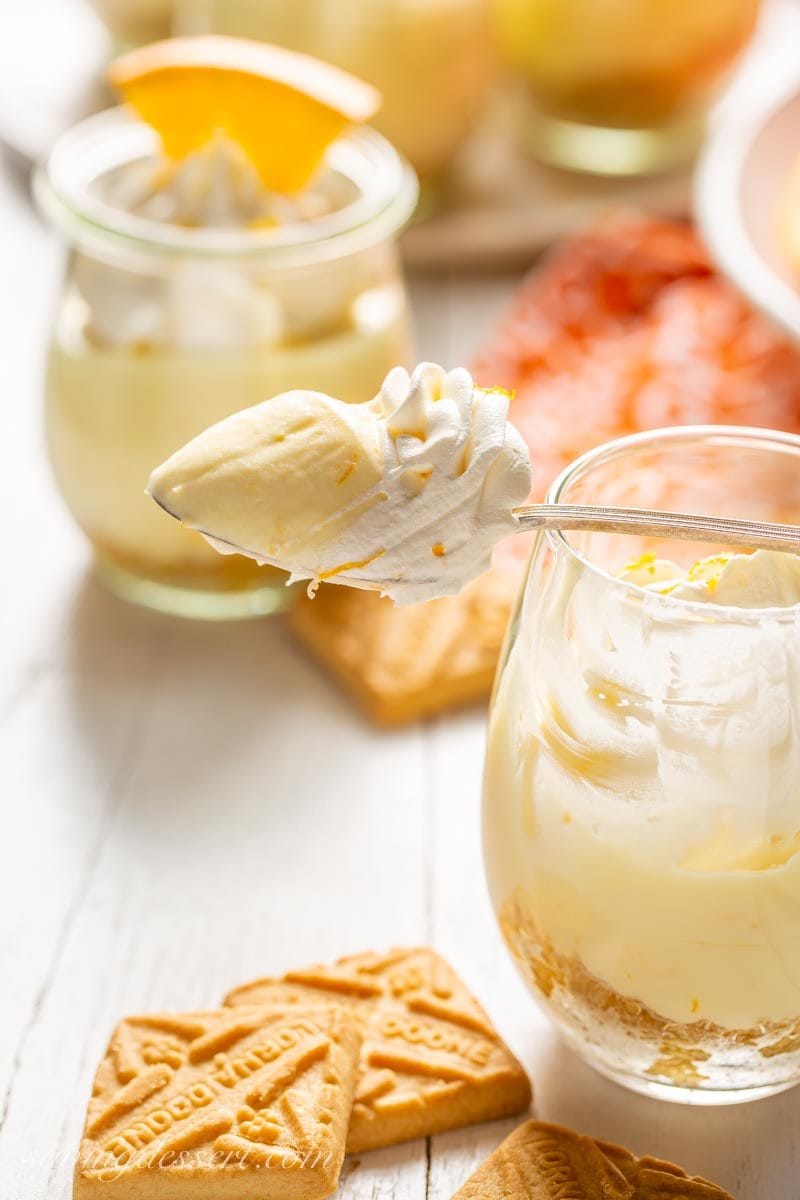 a scoop of Orange Creamsicle No-Bake Cheesecake in a glass with shortbread cookies and orange wedges