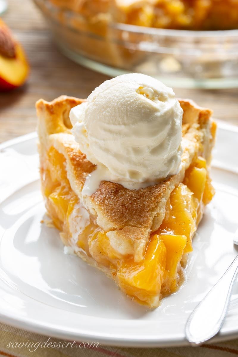 A slice of fresh peach pie with ice cream on top from savingdessert.com