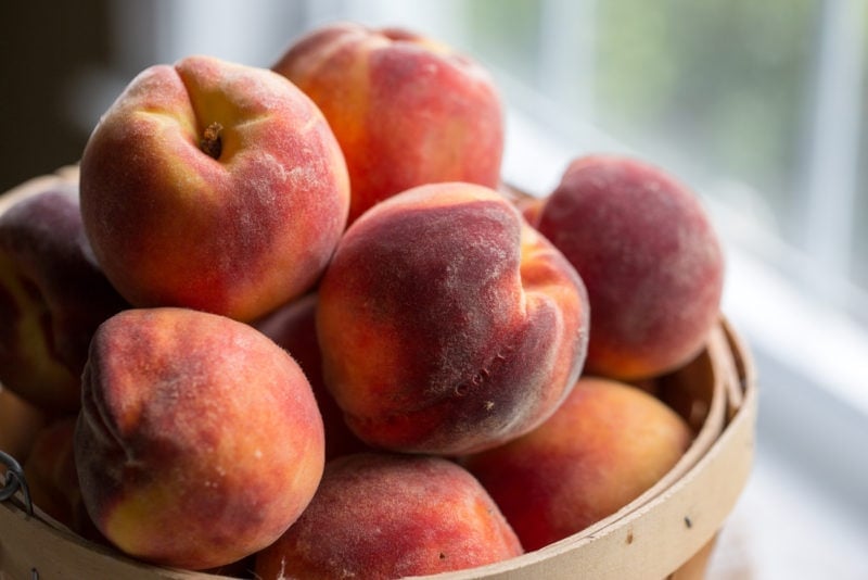 A basket of fresh peaches next to a window