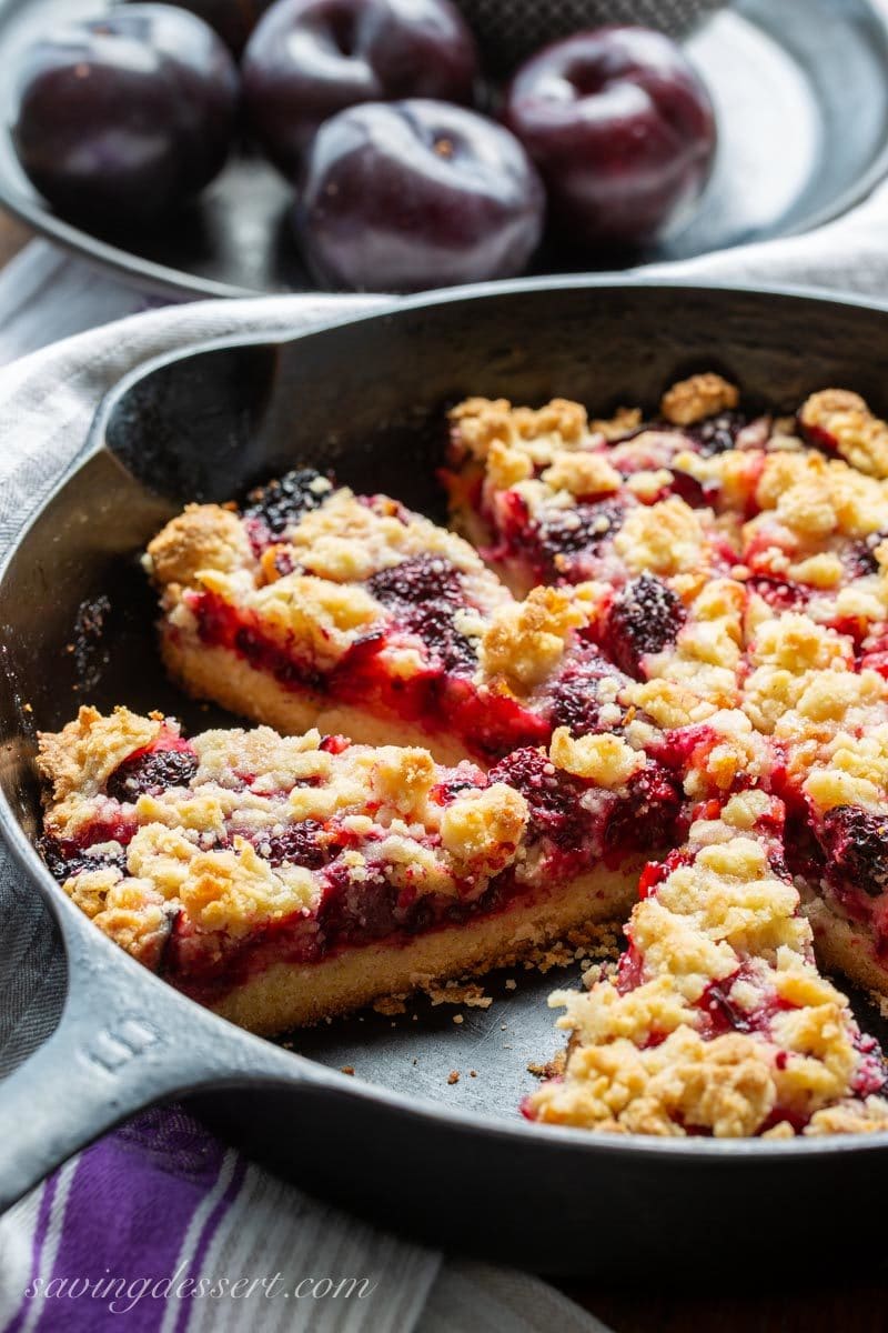 Cast iron skillet with sliced plum blackberry bars and a shortbread crumble dough on top