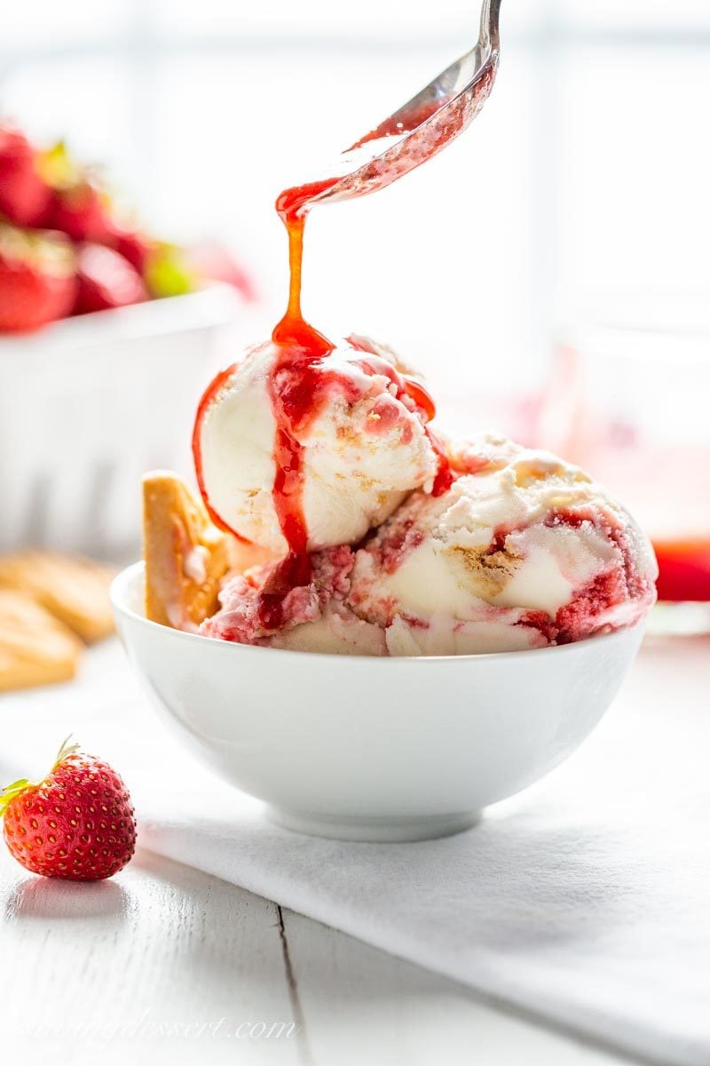 A bowl of strawberry shortcake ice cream being drizzled with strawberry sauce