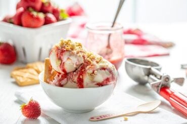 A bowl of strawberry shortcake ice cream with fresh strawberries in the background.