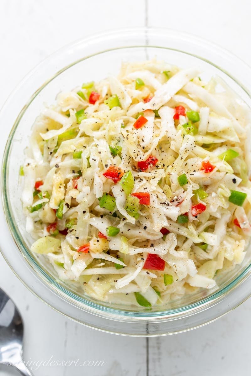 A bowl of mayo-free cabbage slaw with pimentos, onion and chopped green pepper. 