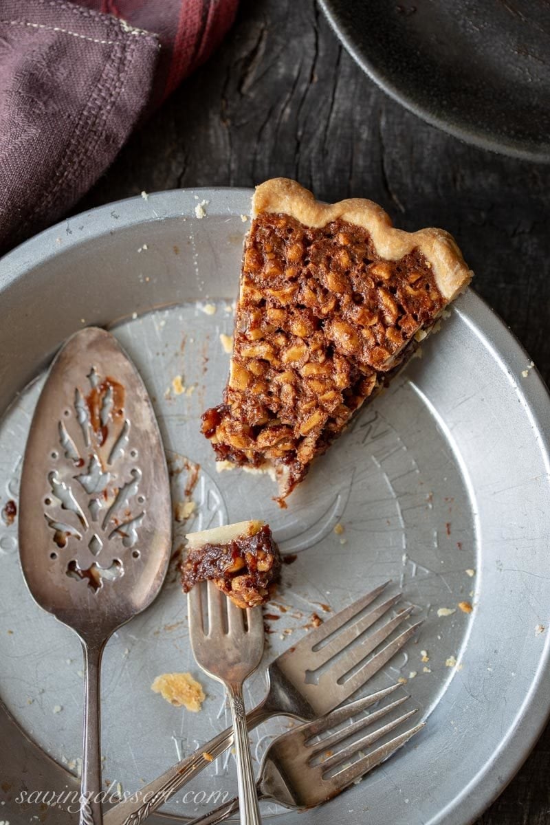 The last slice of chocolate peanut pie in a pie plate with a pie server and extra forks