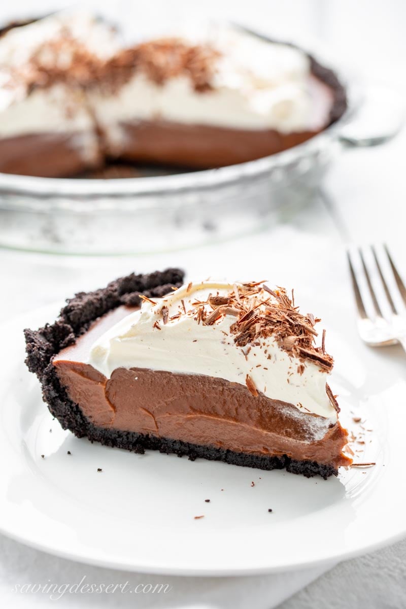 A slice of chocolate pie with a chocolate cookie crust, topped with whipped cream and chocolate shards