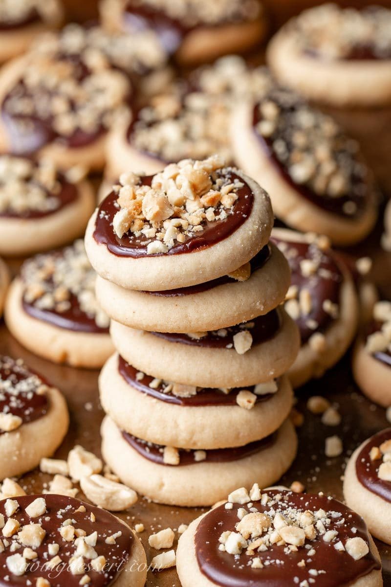 A stack of peanut butter chocolate meltaway cookies with a chocolate glaze and chopped salted peanuts on top