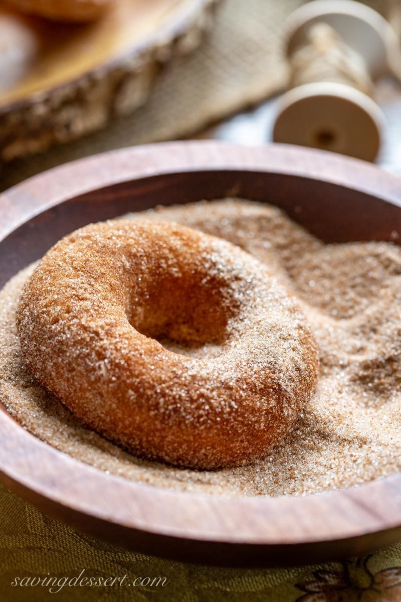 A baked Apple Cider Doughnut tossed in a bowl of cinnamon and sugar